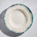 A round gray porcelain wide rim bowl with a speckled design and blue-green edge.