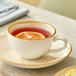 A beige porcelain cup filled with a reddish beverage and a lemon slice, placed on a matching saucer.