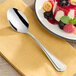 An Acopa Edgeworth stainless steel dessert spoon on a plate with fruit.