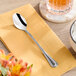 An Acopa Edgeworth stainless steel iced tea spoon on a napkin next to a glass of tea.