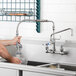 A person using a T&S wall mounted pre-rinse faucet to wash dishes in a sink on a counter in a professional kitchen.