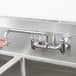 A hand holding a T&S silver wall mounted faucet over a stainless steel sink.