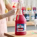 A gallon jug of Carnival King Fruit Punch Snow Cone Syrup with a pump dispenser being used to pour syrup onto a snow cone.