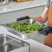A stainless steel food pan filled with green beans being held by a person wearing black gloves.