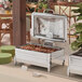 A stainless steel Acopa Manchester chafer stand on a table with food and plates.
