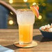An Acopa Memphis highball glass of orange juice with a peach slice on top sits on a table.