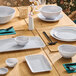 A light gray rectangular melamine platter placed on a wooden dining table set with matching dinnerware.