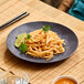 A dark gray round melamine plate with a serving of noodles garnished with lime and cilantro.