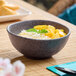 A dark gray round melamine bowl filled with rice, mango, and garnished with mint.