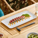 A large white rectangular melamine platter displaying sliced seared tuna with avocado and sauce.