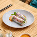 A light gray melamine plate holding two fresh spring rolls with sauce.