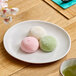 A white round melamine plate holding three pieces of colorful mochi.