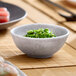 A small, round, light gray melamine bowl filled with green seaweed salad.