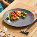 A dark gray round melamine plate with a serving of shrimp, broccoli, rice, and dried red peppers.
