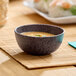 A small dark gray round melamine ramekin filled with soup, placed on a bamboo mat.