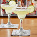 A 9 oz. margarita glass filled with a yellow cocktail, garnished with a lime slice and a salted rim.