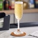 A clear 6 oz. flute glass filled with sparkling beverage, placed on a coaster on a bar counter.
