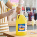 A gallon jug of Carnival King Pineapple Snow Cone Syrup with a pump dispenser being used to flavor a snow cone.