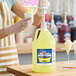 A gallon jug of Carnival King Lemon Snow Cone Flavoring Syrup with a pump dispenser being used to pour syrup onto a snow cone.