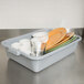 A Tablecraft gray plastic bus tub on a counter with plates and bowls in it.