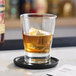 A clear Acopa Fusion 12 oz. rocks glass filled with a brown beverage and ice, placed on a black coaster.