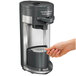 A hand using a Hamilton Beach FlexBrew single serving coffee maker with a removable filter.