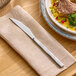 A stainless steel steak knife with a serrated edge placed on a beige napkin.