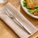 A stainless steel dinner fork with a textured handle resting on a beige napkin.
