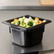 A black Vollrath plastic food pan with vegetables in it on a counter.