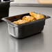A Vollrath black plastic food pan filled with fried chicken on a table.