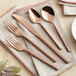 A five-piece set of rose gold stainless steel flatware including two forks, a knife, and two spoons, displayed on a beige napkin.