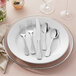 A five-piece set of stainless steel flatware, including two forks, a knife, and two spoons, displayed on a white plate.