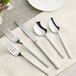 A five-piece set of stainless steel flatware including two forks, a knife, and two spoons.
