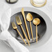 A five-piece set of gold brushed stainless steel flatware displayed on a black plate.