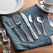 A five-piece set of stainless steel flatware including two forks, a knife, and two spoons, displayed on a blue napkin.