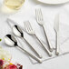 A five-piece set of stainless steel flatware with textured handles, including two spoons, two forks, and a knife.