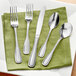 A five-piece set of stainless steel flatware including two forks, a knife, and two spoons, displayed on a green napkin.