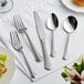 A five-piece set of Acopa Sienna 18/0 stainless steel heavy weight flatware, including two forks, a knife, and two spoons, displayed on a white napkin.