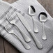 A five-piece set of stainless steel flatware with a hammered handle design, including two forks, a knife, and two spoons, displayed on a white textured cloth.