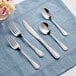 A five-piece set of Acopa Swirl 18/8 stainless steel extra heavy weight flatware displayed on a blue cloth.