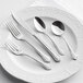 A five-piece set of stainless steel flatware with decorative handles, displayed on a white plate.