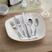 A five-piece set of stainless steel flatware, including two forks, a knife, and two spoons, displayed on a white napkin and plate.