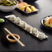 A rectangular stainless steel appetizer tray with an angled brim, shown holding sushi rolls.