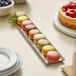 A rectangular stainless steel appetizer tray with an angled brim, shown holding assorted macarons.