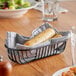A black wire oval basket lined with a gray cloth, holding two breadsticks.