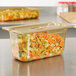 A plastic container of vegetables with a Vollrath 1/3 size amber high heat slotted cover on it.
