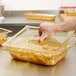 A hand holding a Vollrath amber plastic lid over food in a clear container.