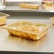 A plastic food container with a Vollrath amber high heat lid on a counter full of food.