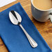 A stainless steel teaspoon with a decorative handle, placed on a blue napkin next to a cup of coffee.