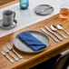 A stainless steel steak knife with a polished finish, placed on a wooden dining table as part of a formal place setting.